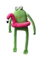 A crocheted green frog toy with large eyes and a pink flamingo float around its body, isolated on a white background. photo