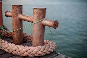Rusty bollards on a dock with thick ropes and green string, close-up of weathered metal, showcasing nautical and maritime equipment in a harbor setting. photo
