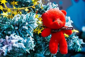 Soft Plush Teddy Bear Ornament Adding a Pop of Red to a Snowy Christmas Tree Setting photo