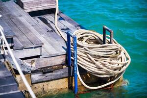 An inviting view of a rustic wooden dock with a neatly coiled rope, set against the stunning backdrop of a turquoise sea, perfect for any nautical-themed design. photo