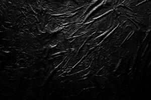 Crumpled black surface with textured wrinkles, abstract dark background. photo