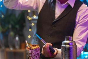 Unrecognizable barman making a cocktail with fire blowtorch flame at party in a nightclub. Nightlife concept. photo