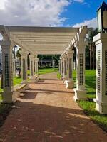 A picturesque path in a garden gracefully winds between elegant columns adorned with beautifully patterned tiles, where sunlight dances through the columns and trees, creating a captivating interplay photo