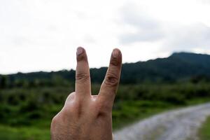 Hand making a peace sign gesture with two fingers raised on a nature background. photo