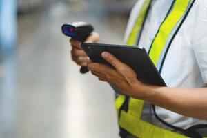 A person in a yellow safety vest is holding a tablet and a barcode scanner. They are likely working in a warehouse or a similar setting where they need to scan items for inventory or tracking purposes photo
