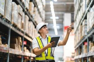 A man in a yellow vest is pointing at a box on a shelf. He is wearing a hard hat and safety glasses photo