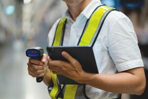 A man wearing a safety vest is holding a tablet and a barcode scanner. He is likely working in a warehouse or a similar environment where he needs to scan items for inventory or tracking purposes photo