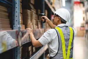 A man in a white shirt and yellow vest is scanning a barcode with a handheld device. He is wearing a hard hat and safety vest, indicating that he is working in a warehouse or industrial setting photo