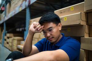 A man in a blue shirt is sitting on a stack of boxes. He is looking down and he is in a state of distress photo