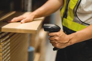 A person is using a barcode scanner in a warehouse. The person is wearing a yellow vest and black pants photo