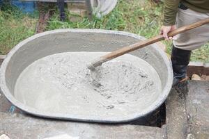 Close up worker using a hoe to mix cement powder, sand, stones in basin for mixing cement. Concept. Construction worker job. Hard working. Process of construction work with cement photo