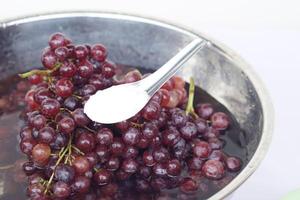 Soak grape fruits in water and spoon of baking soda powder. Concept, cleaning fruits. How to wash grapes for cleanliness and safety before eating. Wash and soak in baking soda water at least 20 minute photo