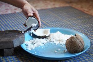 Hands holding a half-cut coconut to scrape for making coconut milk by using coconut grater. Concept Thai cooking style. photo