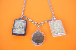 Buddha amulets on orange background. Concept, faith and belief of Buddhist for holy to protect from danger, bring good luck, business prosperity and wealth. Collecting amulet as hobbies or exchange. photo