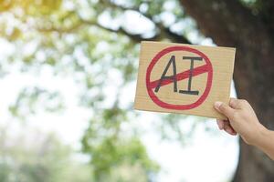Close up hand holds paper card with No AI, prohibition sign. Concept, disagree, anti or don't support or not allow to use AI or Artificial Intelligence in daily life. photo