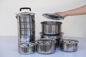 Hand open lid of set of stainless steel cookware and kitchen utensils. Pots, tray and tiffin box for containing food. Concept, safe container for food. photo