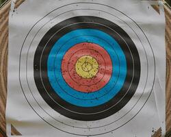 Close-up of a weathered archery target with colorful concentric circles, showcasing signs of use. photo