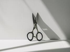 Close-up of a silver scissors resting on a minimalist surface, with dramatic shadows highlighting its shape. photo