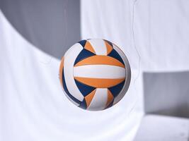 An orange and blue volleyball suspended in mid-air against a soft white background. photo