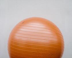 An orange exercise ball positioned against a minimalistic white wall. photo