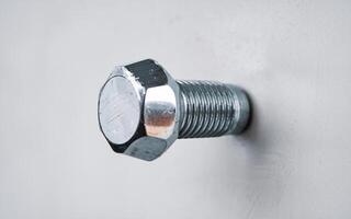 Close-up of a shiny steel bolt embedded in a light background, showcasing its texture and detail. photo