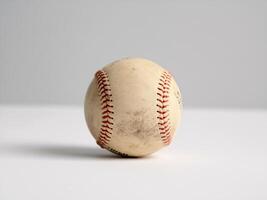 Close-up of a worn baseball with visible scuff marks and red stitching on a gray background. photo