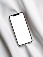 A sleek smartphone resting on smooth white fabric, showcasing its blank screen. photo