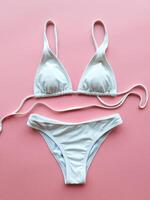 Stylish white bikini set laid out on pink backdrop, perfect for summer beach days. photo