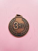 Bronze medal with '3RD' in the center, set against a soft pink background, symbolizing achievement. photo