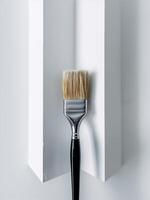 A close-up of a paintbrush resting against a pristine white wall, symbolizing creativity and DIY projects. photo