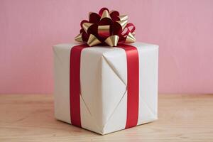 Beautifully wrapped gift box with a red ribbon and bow, set against a soft pink background. photo