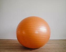 A bright orange exercise ball positioned against a plain wall, adding a pop of color to the room. photo