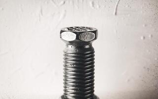 Close-up of a metallic bolt, showcasing its detailed threads and hexagonal head against a textured background. photo