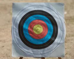A close-up of a well-used archery target with colorful concentric circles and numerous arrow marks. photo