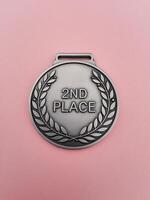 A silver medal with '2ND PLACE' inscribed in bold letters, set against a soft pink background. photo