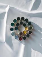 A vibrant circle of paint pots in assorted colors arranged artistically on a white fabric surface. photo