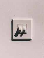 Close-up of a white electrical switch on a textured wall, casting soft shadows. photo