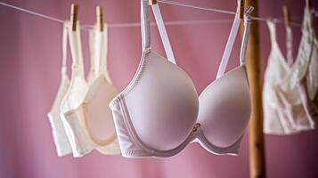 A row of white and cream bras hanging on a clothesline with a soft pink background. photo