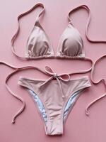 Stylish pink bikini set featuring a triangle top and adjustable tie bottoms on a soft pink backdrop. photo