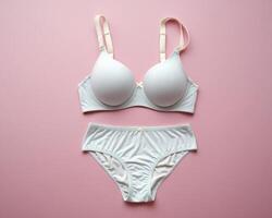 Elegant white bra and panty set displayed on a soft pink background, showcasing a minimalist design. photo
