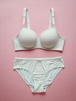 Elegant white lingerie set displayed on a soft pink background, emphasizing the delicate design. photo