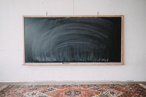 Empty blackboard in a minimalist classroom setting, framed by wooden accents and a vintage rug. photo