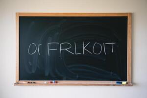 A blank chalkboard with the letters 'OF FRLKCOIT' scribbled in white chalk, creating a creative and playful mood. photo