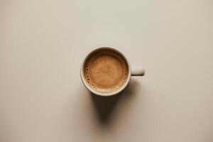 A simple white coffee cup filled with creamy coffee, set against a soft neutral background. photo