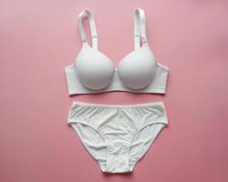 Elegant white lingerie set displayed on a soft pink background, showcasing its smooth contours and delicate design. photo