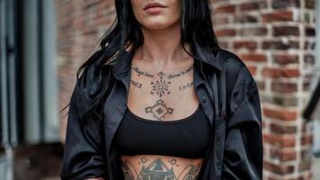 Close-up woman's chest tattoos, intricate designs and script. Urban backdrop. Ideal for showcasing body art and alternative fashion. photo
