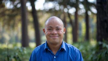 Man with Down syndrome smiling joyfully outdoors in park setting evokes feelings of connection with nature and inclusion. Community concept photo