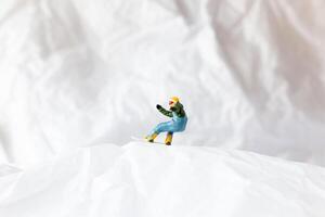 Miniature people snowboarder dressed in vibrant winter gear, carving through a snowy slope photo