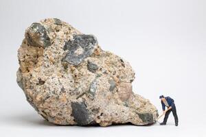 Miniature worker using a pickaxe to chip away at a large rock photo