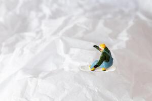 Miniature people snowboarder dressed in vibrant winter gear, carving through a snowy slope photo